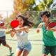Nhóm thanh niên Việt Nam đang chơi pickleball trên sân ngoài trời, hành động đánh bóng sôi nổi dưới nắng, trang phục thể thao năng động, không có chữ trong ảnh